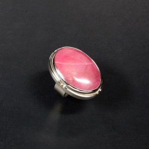 May include: A silver ring with a large oval pink gemstone set in a silver bezel.