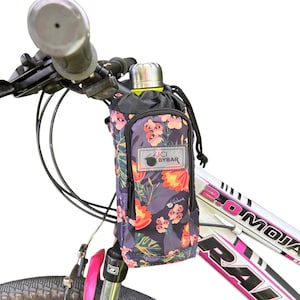 May include: A bicycle handlebar bag featuring a dark floral pattern with pink, orange, and green leaves. The bag has a drawstring top, a front zippered pocket, and a rectangular patch with the text BICI BYBAR. A silver water bottle is inside.