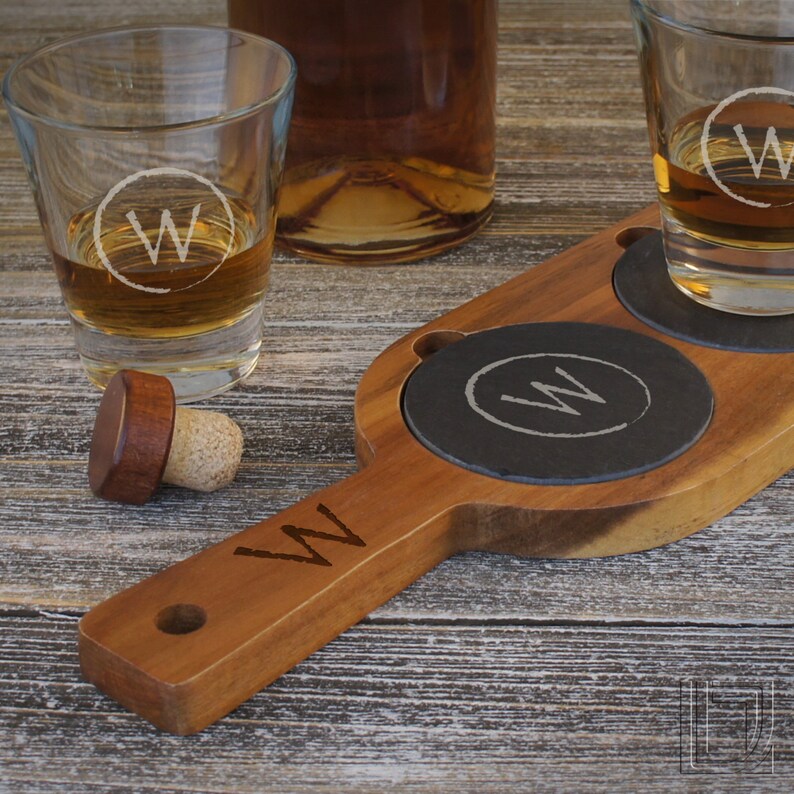 May include: Wooden serving tray with two round black slate coasters. Each coaster has a white circle with the letter "W" in the centre. The tray has a handle and is engraved with the letter "W".