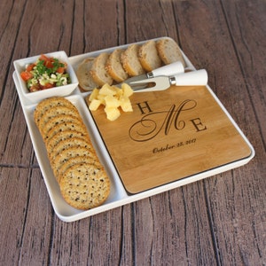 May include: A white serving tray with a removable bamboo cutting board. The cutting board has a personalized message that reads "H & M E October 28, 2017". The tray has compartments for crackers, cheese, and a small bowl for dip.