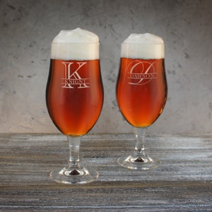 May include: Two personalized beer glasses with a frosted finish. The glass on the left has the letter "K" and the name "Knight" etched on it. The glass on the right has the letter "D" and the name "Dawson" etched on it.