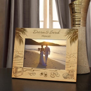 May include: A wooden photo frame with a tropical theme. The frame has a cutout of palm trees, a cruise ship, sunglasses, flip flops, and a coconut drink. The frame is personalized with the names "Darren & Sarah" and the location "Hawaii". The year "2020" is also engraved on the frame.