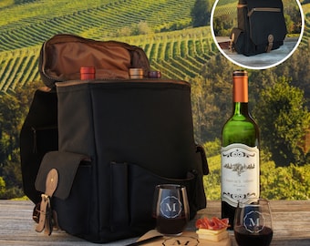 May include: Black canvas wine backpack with a brown leather trim. The backpack has a zippered compartment, a bottle holder, and two insulated pockets. The backpack is open and shows two wine bottles inside. The backpack is sitting on a wooden table with a wine bottle, two wine glasses, a cutting board, a cheese knife, and a corkscrew.