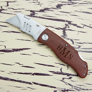 May include: A brown wooden handled utility knife with a silver blade. The handle is engraved with the initials "HMN".