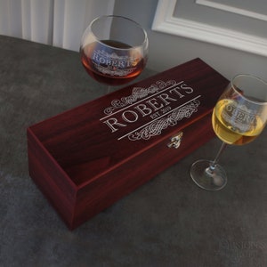 May include: A wooden box with a hinged lid engraved with the text "ROBERTS EST. 2019" and a decorative design. Two wine glasses are also shown, one with red wine and the other with white wine.