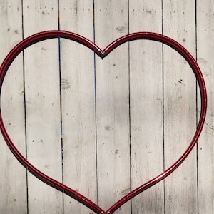May include: A red heart-shaped metal hoop is attached to a white wooden fence. The hoop is made of thin metal and is slightly bent in the middle. The fence is made of vertical wooden planks.