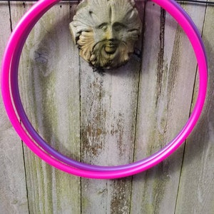 May include: A pink and purple plastic hula hoop hanging on a wooden fence.