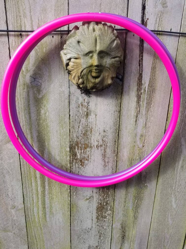 May include: A pink and purple plastic hula hoop hanging on a wooden fence.