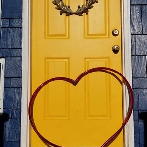 May include: A yellow door with a wreath and a red heart-shaped decoration in front of it.
