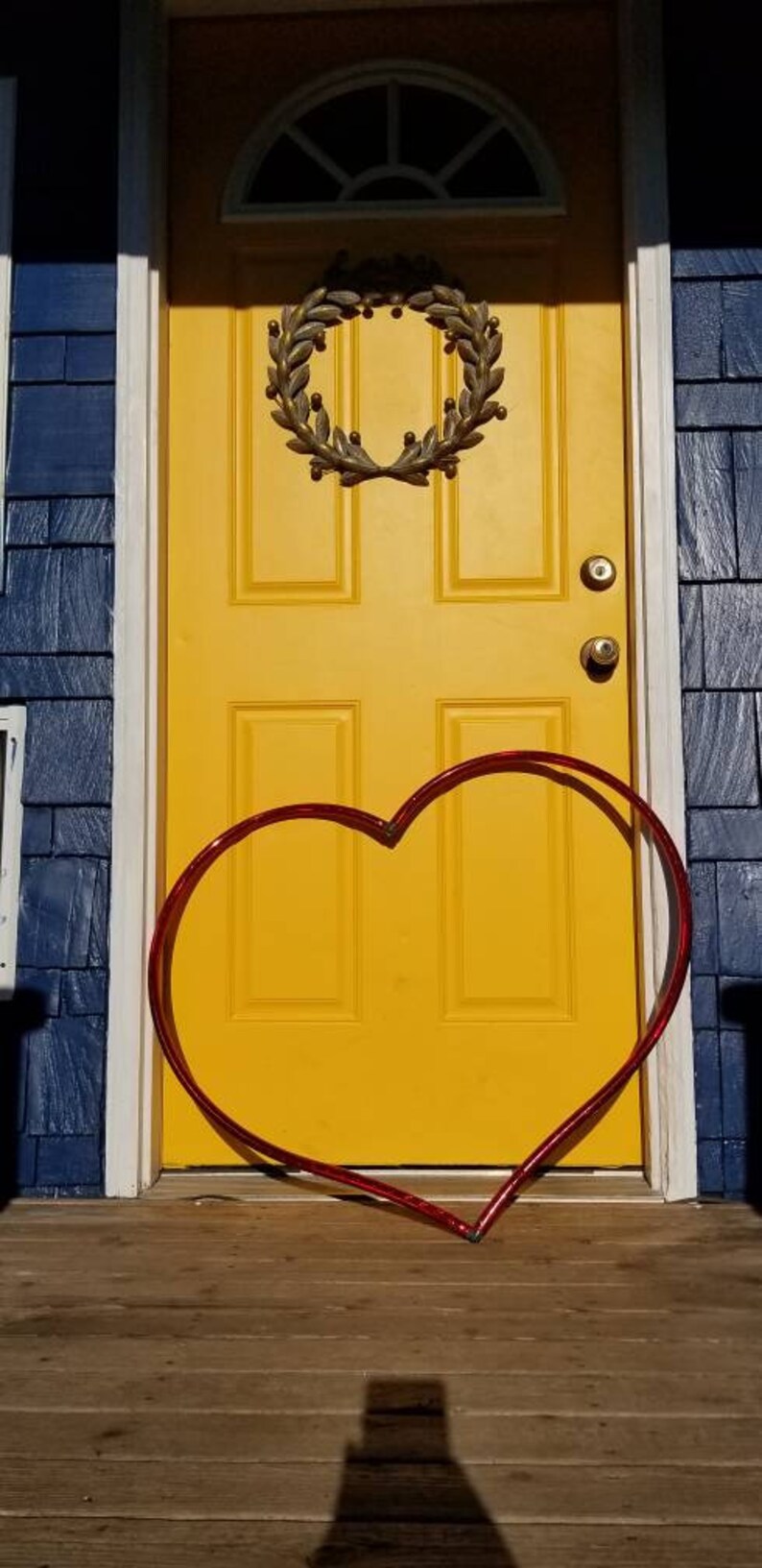 May include: A yellow door with a wreath and a red heart-shaped decoration in front of it.