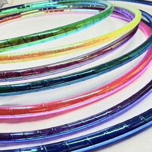 Op de afbeelding: Een set van regenboogkleurige, iriserende plastic hoelahoepringen. De ringen zijn op elkaar gestapeld, met de blauwe ring onderaan en de groene ring bovenaan.