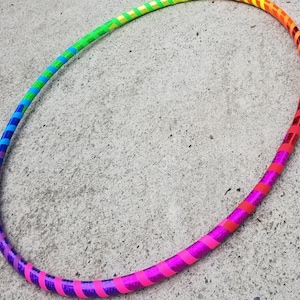 Könnte beinhalten: Ein farbenfroher Hula-Hoop-Reifen mit einem Regenbogen-Farbverlauf. Der Reifen wechselt von Lila zu Pink, Rot, Orange, Gelb, Grün und Blau. Der Reifen besteht aus einem glänzenden, reflektierenden Material.