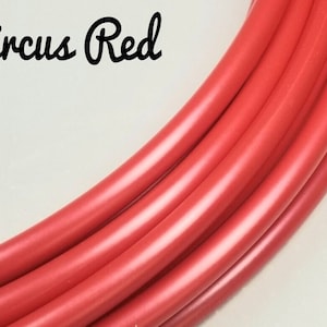 Puede incluir: Primer plano de un tubo rojo brillante, posiblemente para manualidades o equipos de ejercicio. El texto "Circus Red" está escrito en cursiva. El tubo es liso y parece estar hecho de un material flexible.