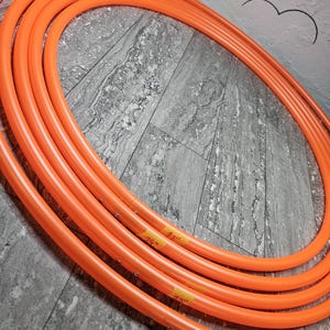 Puede incluir: Varios aros de hula naranja, etiquetados con cinta amarilla. Los aros están dispuestos en un patrón circular, con etiquetas que indican tamaños como 74 cm y 56 cm. Los aros están hechos de un material liso y flexible.