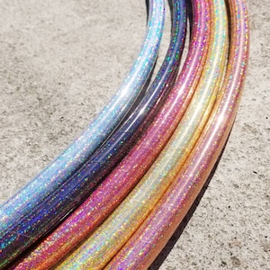 May include: A set of six iridescent glitter hula hoops in various colours, including silver, pink, gold, and orange. The hoops are arranged in a semi-circle, with the silver hoop at the top and the orange hoop at the bottom.