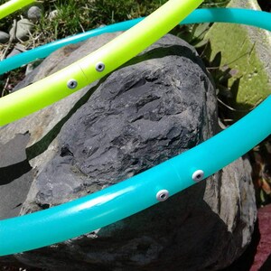 May include: Two plastic hula hoops, one green and one yellow, are resting on a large gray rock. The hoops have white plastic accents.