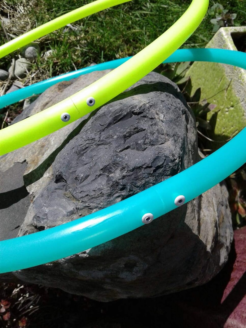 May include: Two plastic hula hoops, one green and one yellow, are resting on a large gray rock. The hoops have white plastic accents.