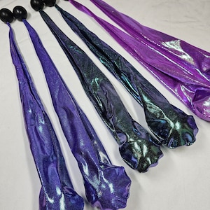 Op de afbeelding: Zes iriserende paarse en groene stoffen streamers met zwarte gewogen ballen aan het einde.