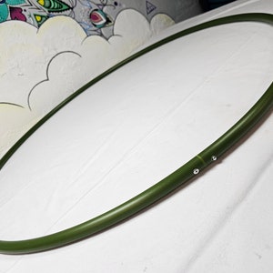 Könnte beinhalten: Ein olivgrüner, oval geformter Reifen, möglicherweise zum Basteln oder Dekorieren, wird vor einem weißen Hintergrund gezeigt. Der Reifen besteht aus einem glatten, festen Material und ist mit kleinen silbernen Befestigungen verbunden.