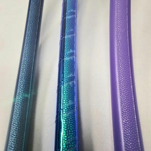 K&ouml;nnte beinhalten: Nahaufnahme von drei farbenfrohen Hula-Hoops. Die Reifen sind in Blau- und Lilat&ouml;nen gehalten und mit strukturiertem Griffband versehen. Das Bild zeigt die gebogene Form der Reifen und die detaillierte Textur des Bandes.