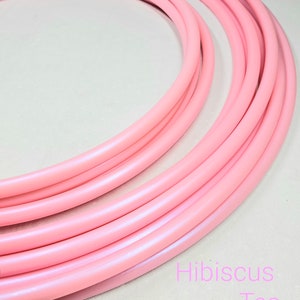 May include: A set of pink plastic hula hoops, stacked on top of each other. The hoops are a light pink color with a slight shimmer. The text "Hibiscus Tea" is written in pink letters on the bottom right corner of the image.