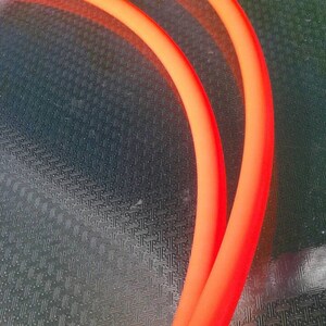 May include: Two orange neon tubes bent into a semi-circle shape, lying on a textured surface.