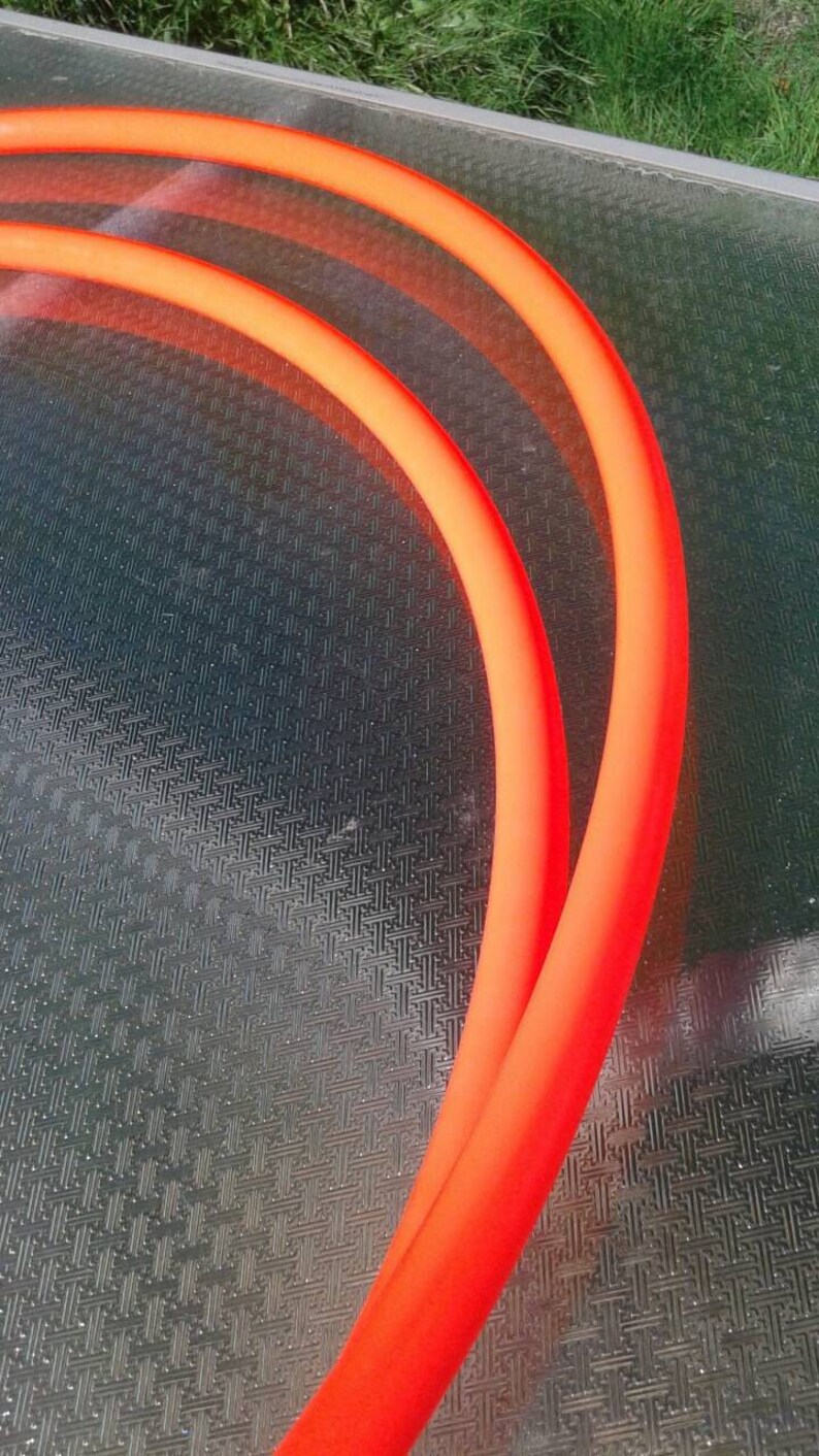 May include: Two orange neon tubes bent into a semi-circle shape, lying on a textured surface.