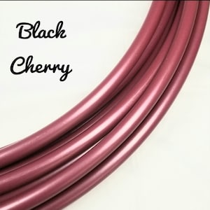 Könnte beinhalten: Nahaufnahme von mehreren gebogenen, glänzenden, schwarz-kirschfarbenen Rohren. Die Rohre sind in einem Halbkreis vor einem weißen Hintergrund angeordnet. Die Worte "Black Cherry" sind in kursiver Schrift in der oberen linken Ecke geschrieben.