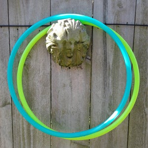 May include: Two plastic hoops, one green and one blue, are intertwined and hanging on a wooden fence. The hoops are both circular and appear to be made of flexible plastic.