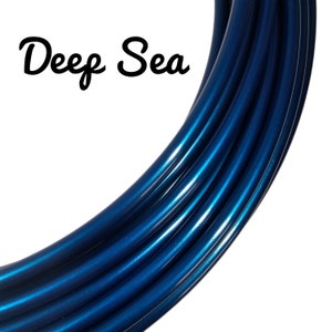Könnte beinhalten: Nahaufnahme eines gebogenen, glänzenden, tiefblauen Objekts. Das Objekt hat einen metallischen Glanz und reflektiert das Licht, wodurch Glanzlichter entstehen. Der Text "Deep Sea" ist in Schwarz in Schreibschrift geschrieben.
