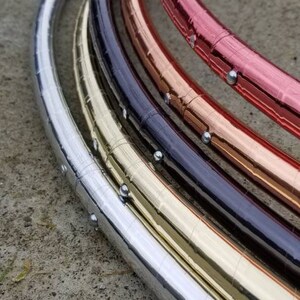 May include: Five hoop rings stacked on top of each other. The rings are made of metal and are silver, gold, copper, black, and red.