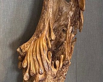May include: A tall, abstract wooden sculpture with a natural, weathered appearance. The sculpture is mounted on a black metal base and features intricate, organic carvings and a warm, brown color.