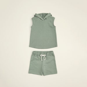May include: A sage green sleeveless hoodie and matching shorts set for kids. The hoodie has a drawstring hood and the shorts have a drawstring waist.