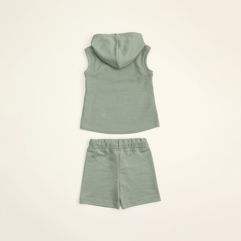 May include: A sage green sleeveless hoodie and matching shorts set for kids. The hoodie has a drawstring hood and the shorts have an elastic waistband.