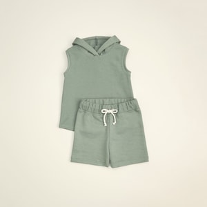 May include: A sage green sleeveless hoodie and matching drawstring shorts set for kids. The hoodie has a drawstring hood and the shorts have a relaxed fit.