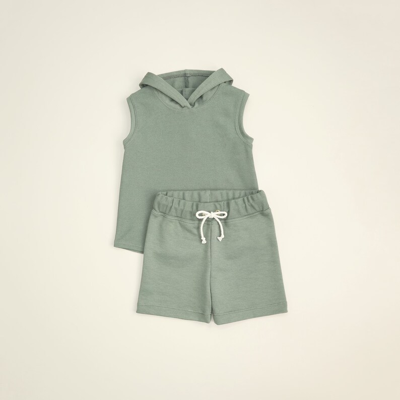 May include: A sage green sleeveless hoodie and matching drawstring shorts set for kids. The hoodie has a drawstring hood and the shorts have a relaxed fit.
