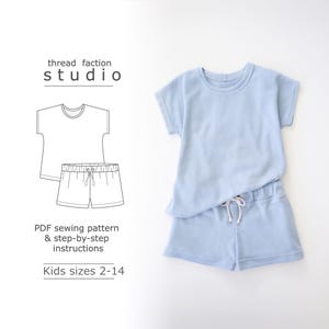 Può includere: Un cartamodello per un set di maglietta a maniche corte e pantaloncini per bambini. Il cartamodello è per le taglie 2-14. L'immagine mostra un set di maglietta e pantaloncini di colore azzurro.