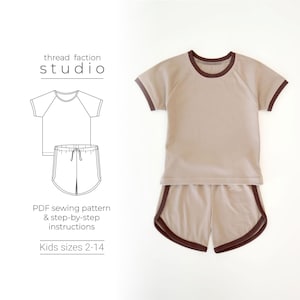 Op de afbeelding: Een naaipatroon voor een kinder T-shirt en shorts set. Het patroon bevat instructies voor maten 2-14. Het T-shirt heeft een bruine bies rond de hals en mouwen. De shorts hebben een bruine bies rond de tailleband en benen.