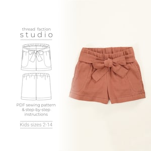 May include: A sewing pattern for kids shorts with a bow tie. The pattern includes instructions for sizes 2-14. The image shows a line drawing of the shorts and a photo of the finished product in a terracotta color.