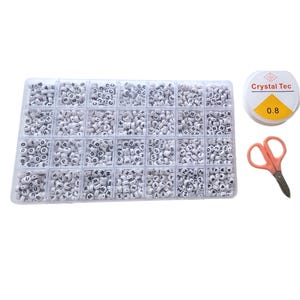 Puede incluir: Un organizador de plástico transparente lleno de cuentas de alfabeto blancas con letras negras. También se incluyen una bobina de hilo Crystal Tec de 0,8 mm y unas tijeras naranjas. Ideal para la fabricación de joyas y manualidades.