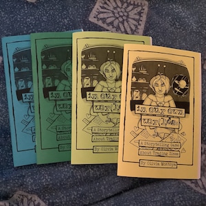Könnte beinhalten: Vier Zines mit farbigen Umschlägen, die jeweils den Titel "in our own worlds" und eine Zeichnung einer Person mit spitzen Ohren zeigen. Der Text darunter lautet "A Storytelling Game About Trading Zines" von Olivia Montoya. Die Umschläge sind blau, grün und gelb.