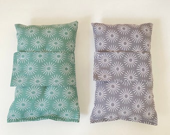 Puede incluir: Dos pequeñas almohadas rectangulares con un patrón de estrellas blancas sobre un fondo verde y gris. Las almohadas tienen una solapa que se puede doblar para crear un bolsillo.