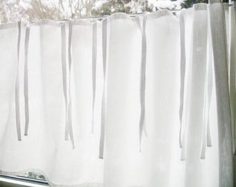 Puede incluir: Cortinas blancas transparentes con rayas verticales grises y lazos. Las cortinas cuelgan frente a una ventana, creando una luz suave y difusa. La tela parece ligera y aireada, adecuada para un dormitorio o sala de estar.