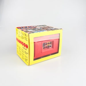 May include: A yellow box containing a red and black toy camera. The box features a picture of a group of people on the front and the words "Photomat" and "Instructions" on the side.