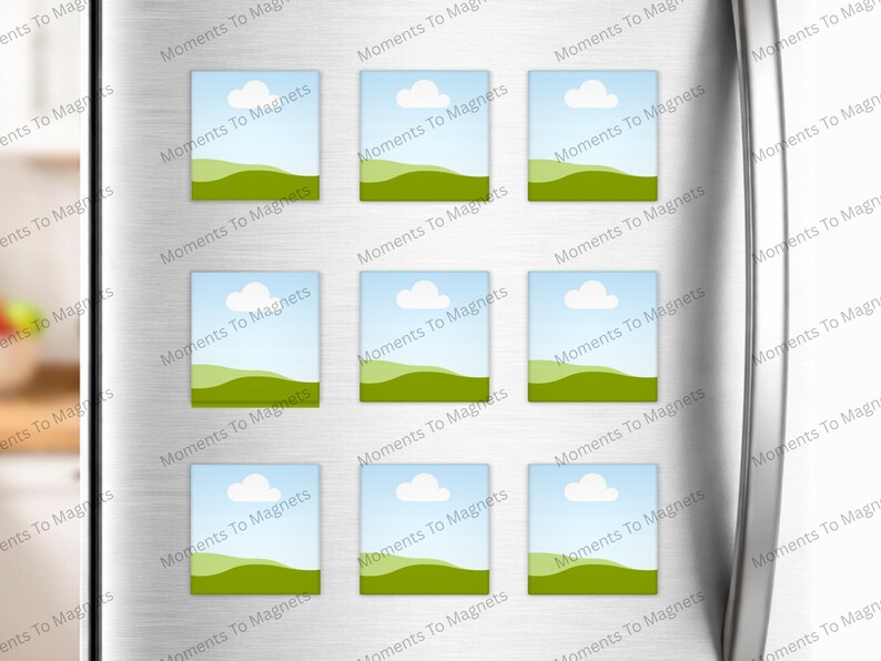 May include: Nine rectangular magnets with a landscape design are displayed on a silver refrigerator door. Each magnet features a blue sky with a white cloud, green hills, and the text "Moments To Magnets".