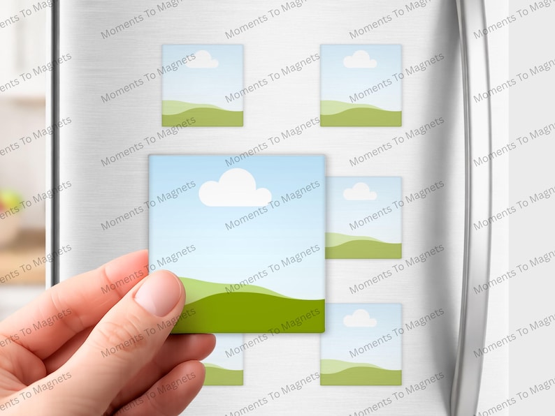 May include: A hand holding a square magnet with a landscape design of a blue sky, white cloud, and green hills. Several similar magnets are attached to a refrigerator. The text "Moments To Magnets" is printed on the magnets.