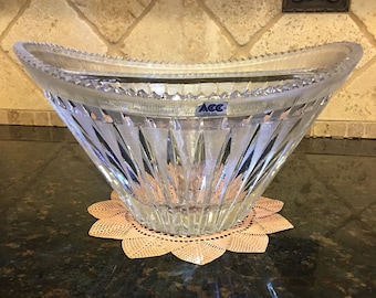 May include: A clear glass bowl with a scalloped rim and a diamond pattern. The bowl is sitting on a brown lace doily. The bowl has a blue label that says "ACC" on it.