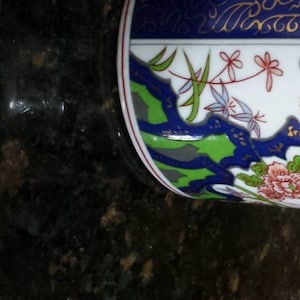 May include: A decorative white ceramic teapot with a bamboo handle. The teapot features a floral design with red, blue, and green accents. The spout and handle are white with gold trim. The lid has a floral pattern.