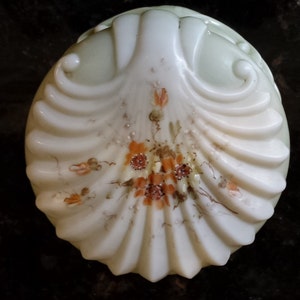 May include: A white porcelain trinket box shaped like a seashell with a raised design and painted with orange and brown flowers.