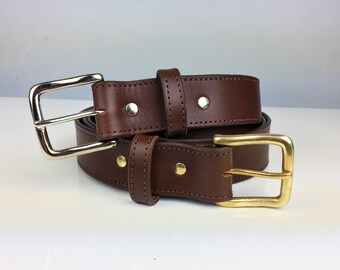 May include: A brown leather belt with a silver buckle and a brass buckle. The belt is folded in half and the buckles are visible.